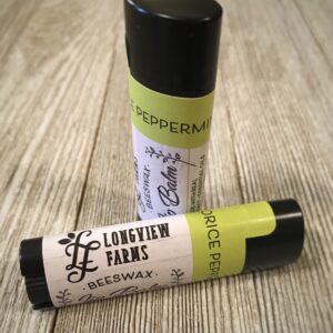 Two Longleaf Farms lip balms on a wood surface, one upright and one lying down.