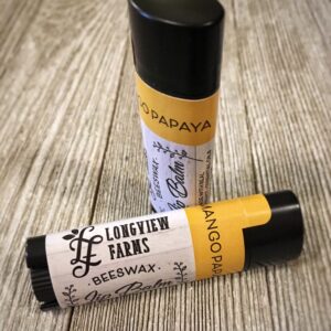 Two lip balm tubes labeled 'Longterm Love' and 'Smooch' on a wooden surface.