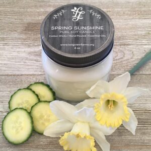 A jar of body cream with cucumber slices and white flowers on wooden surface.
