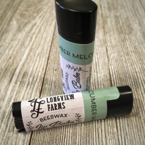 Two small containers of Longview Farms beeswax lip balm on a wooden surface.