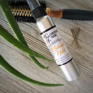 A silver bottle of skincare serum on a wooden surface with green leaves nearby.