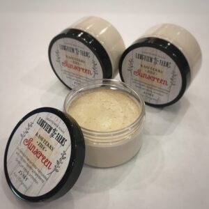 Three jars of homemade skincare cream with one open showing the cream.
